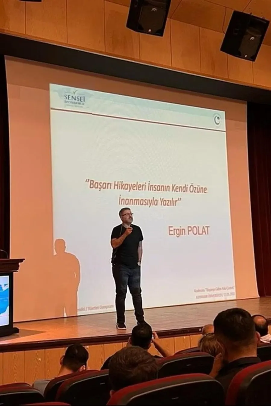 Ergin Polat konferansta konuşma yaparken; perdede “Başarı hikâyeleri insanın kendi özüne inanmasıyla yazılır” yazıyor